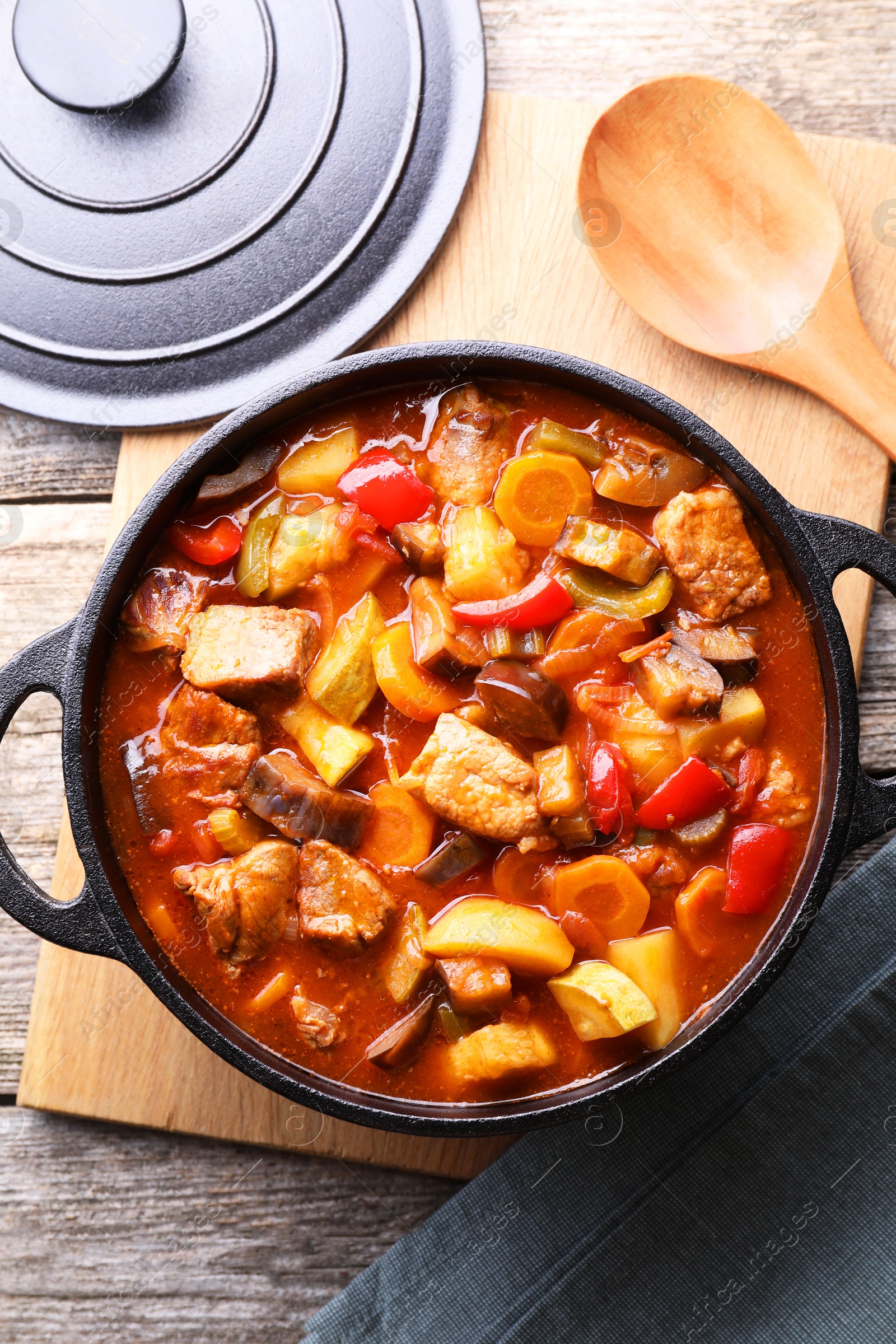 Photo of Delicious stew with vegetables in pot and spoon on wooden table, top view