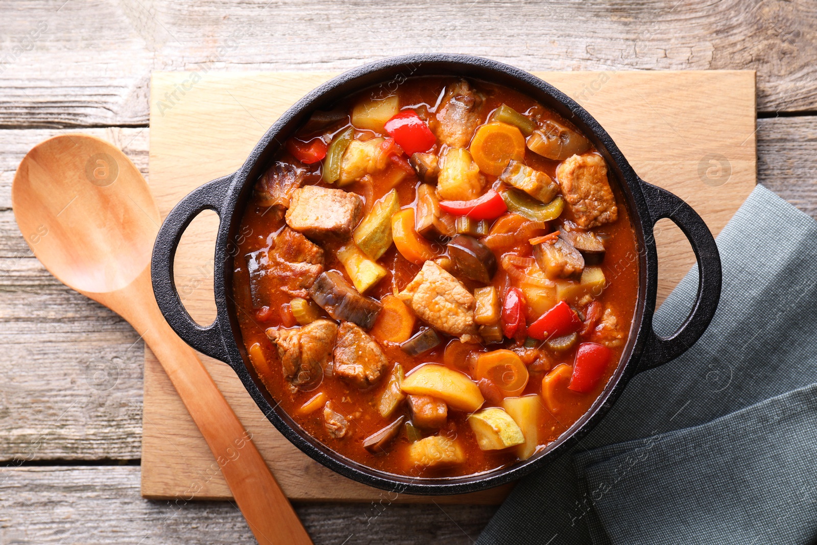 Photo of Delicious stew with vegetables in pot and spoon on wooden table, top view