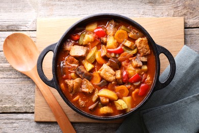 Delicious stew with vegetables in pot and spoon on wooden table, top view