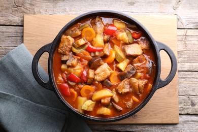 Delicious stew with vegetables in pot on wooden table, top view