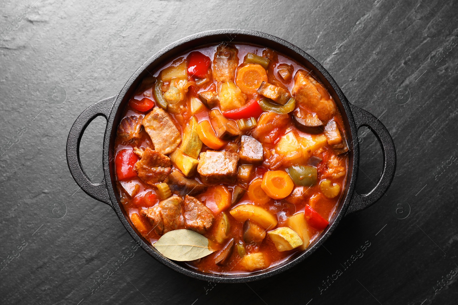 Photo of Delicious stew with vegetables in pot on gray textured table, top view