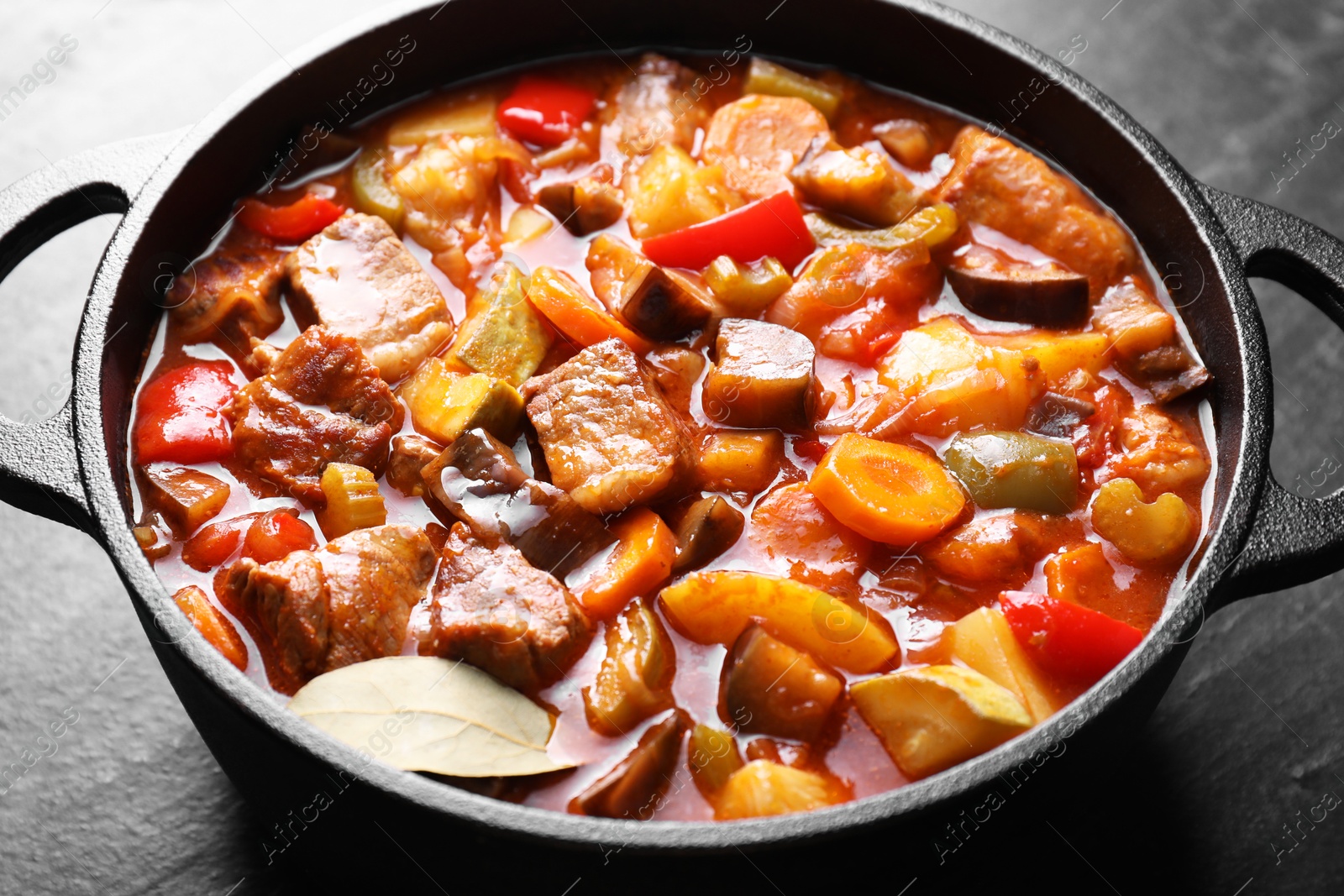 Photo of Delicious stew with vegetables in pot on gray textured table, closeup