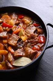 Delicious stew with vegetables in pot on gray textured table, closeup