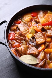 Photo of Delicious stew with vegetables in pot on gray textured table, closeup