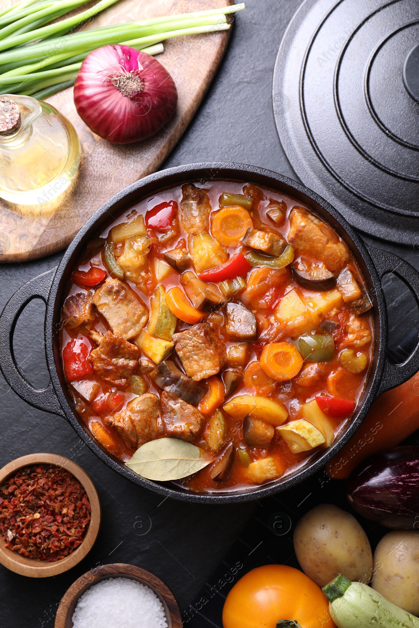 Photo of Delicious stew with vegetables in pot and ingredients on gray textured table, flat lay