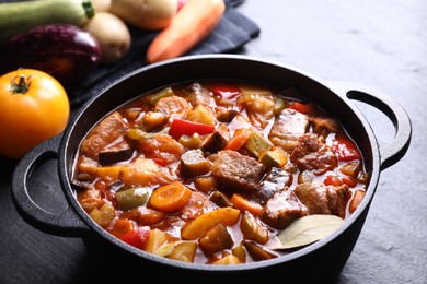 Photo of Delicious stew with vegetables in pot and ingredients on gray textured table, closeup