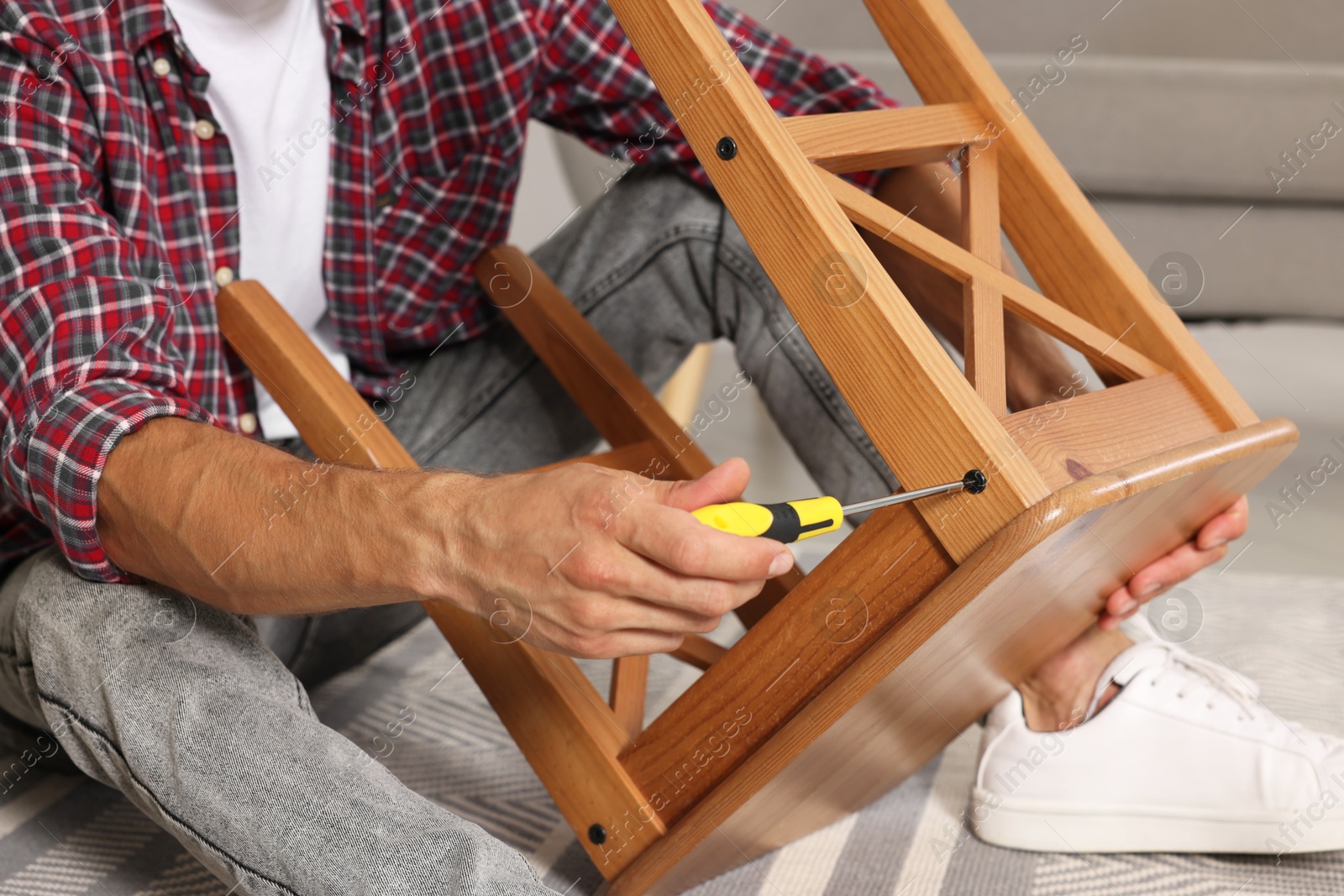 Photo of Man repairing wooden stool with screwdriver indoors, closeup