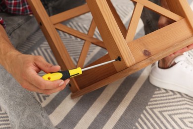 Man repairing wooden stool with screwdriver indoors, closeup