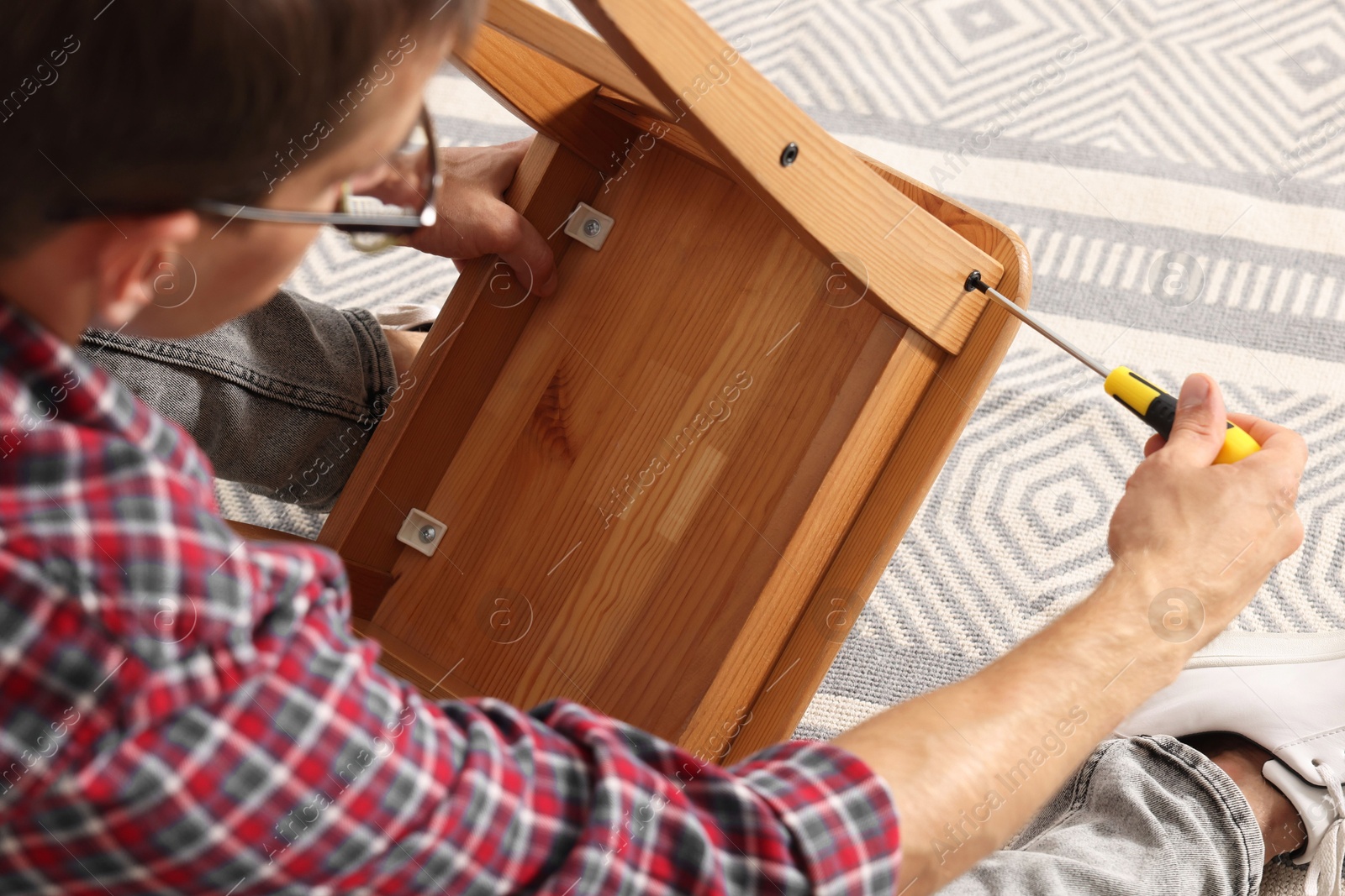 Photo of Man repairing wooden stool with screwdriver indoors, closeup