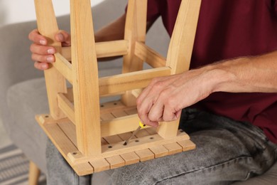 Man repairing wooden stool with screwdriver indoors, closeup