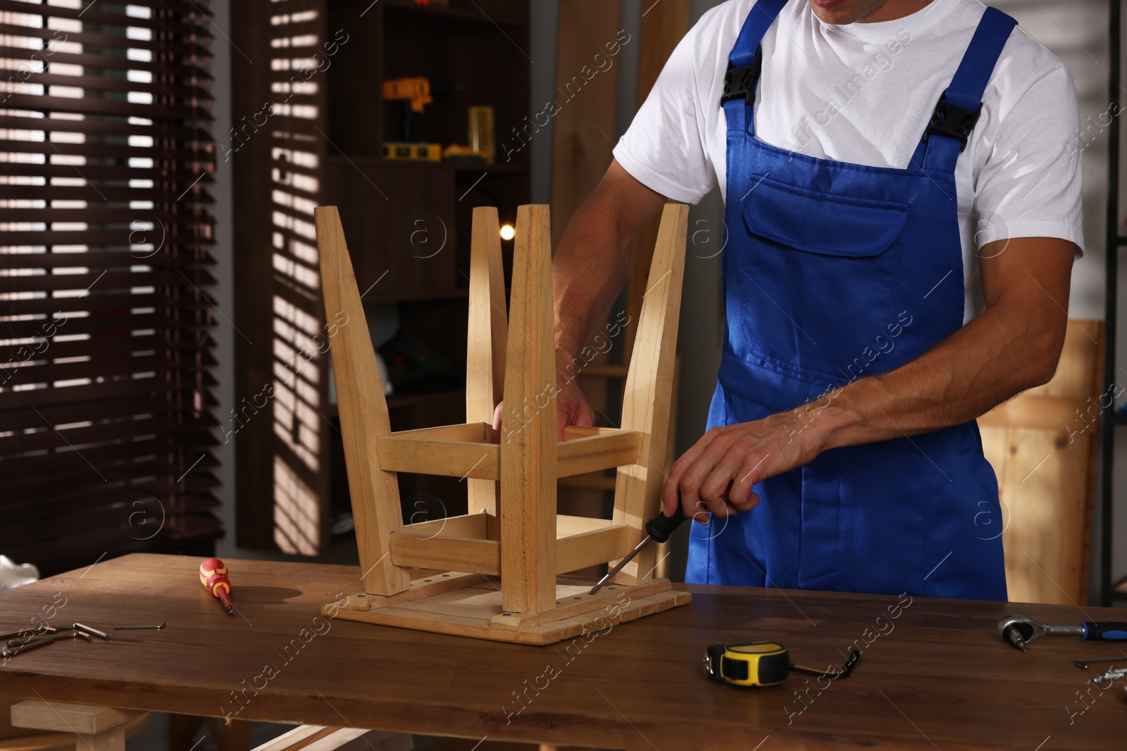 Photo of Man repairing wooden stool with screwdriver indoors, closeup