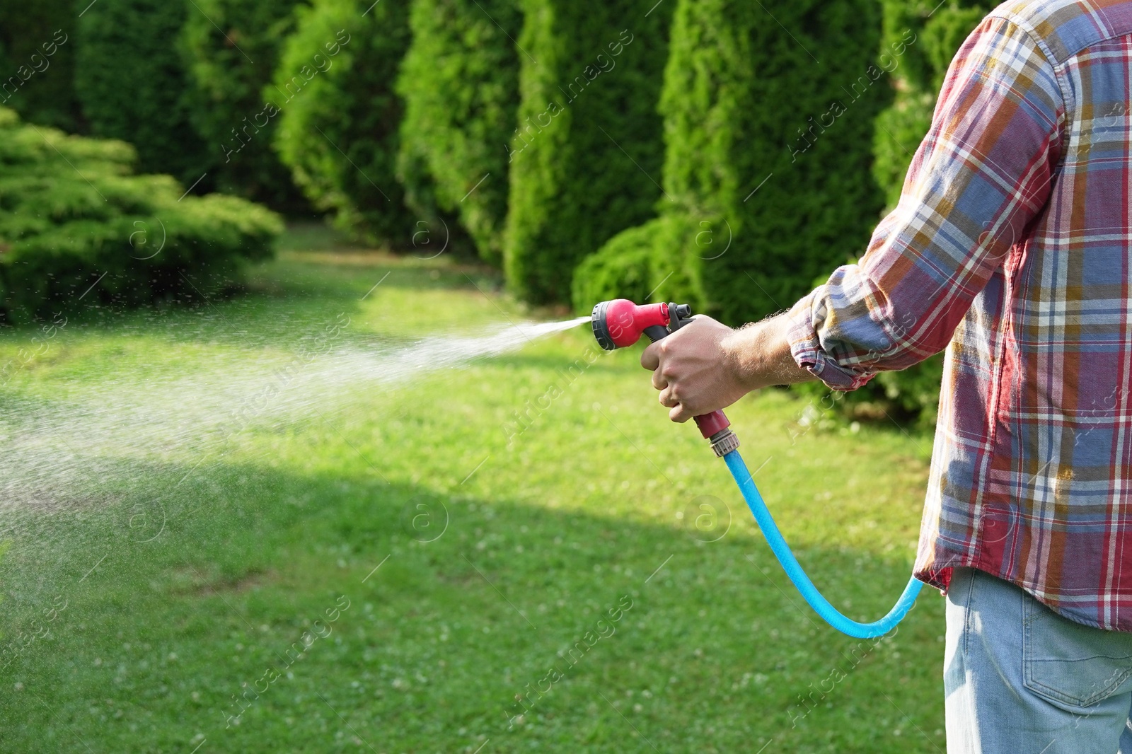 Photo of Man watering lawn with hose in backyard, closeup