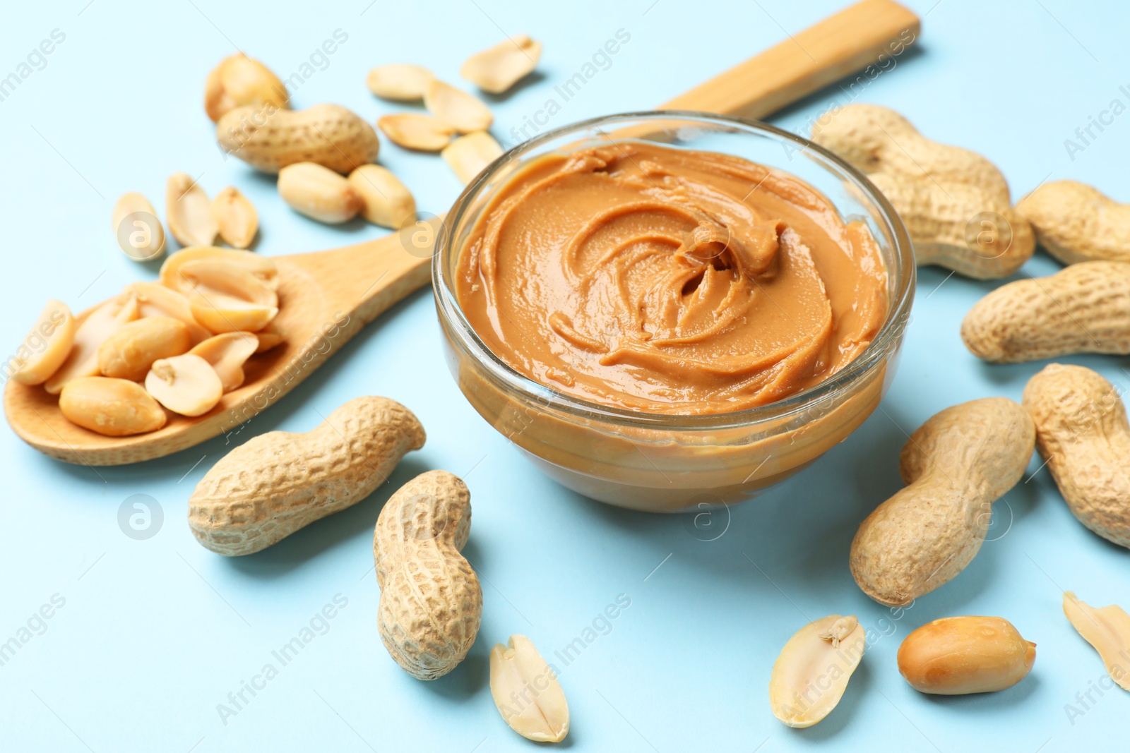 Photo of Tasty peanut butter and groundnuts on light blue background, closeup