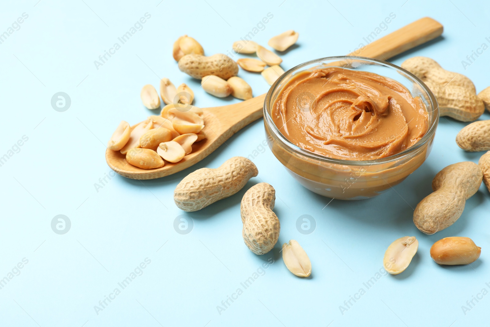 Photo of Tasty peanut butter in bowl and groundnuts on light blue background, space for text