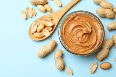 Photo of Tasty peanut butter and groundnuts on light blue background, flat lay. Space for text