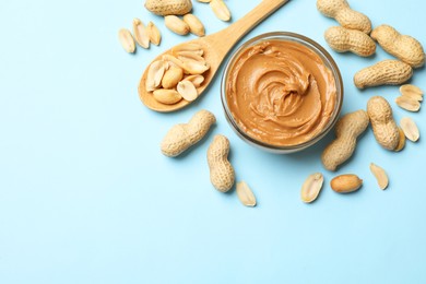 Photo of Tasty peanut butter and groundnuts on light blue background, flat lay. Space for text