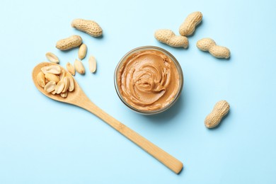 Photo of Tasty peanut butter and groundnuts on light blue background, flat lay