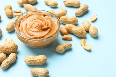 Photo of Tasty peanut butter in bowl and groundnuts on light blue background, closeup