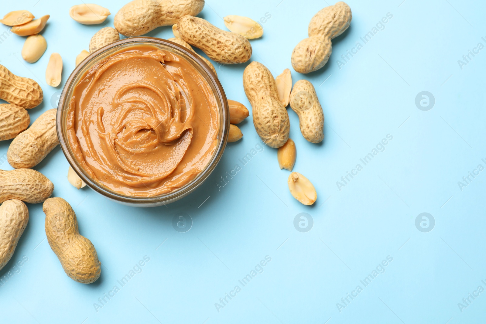 Photo of Tasty peanut butter in bowl and groundnuts on light blue background, flat lay. Space for text