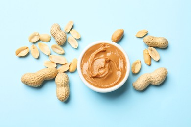 Photo of Tasty peanut butter in bowl and groundnuts on light blue background, flat lay