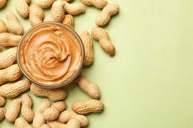 Tasty peanut butter in bowl and groundnuts on pistachio color background, flat lay. Space for text