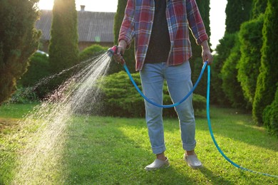 Man watering green grass on lawn in backyard, closeup