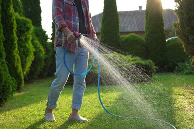 Photo of Man watering green grass on lawn in backyard, closeup