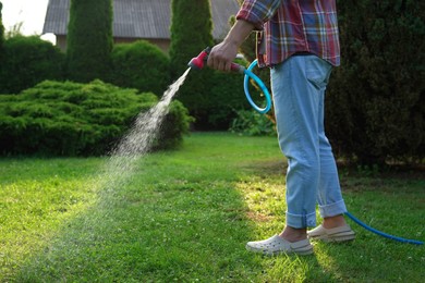 Man watering green grass on lawn in backyard, closeup