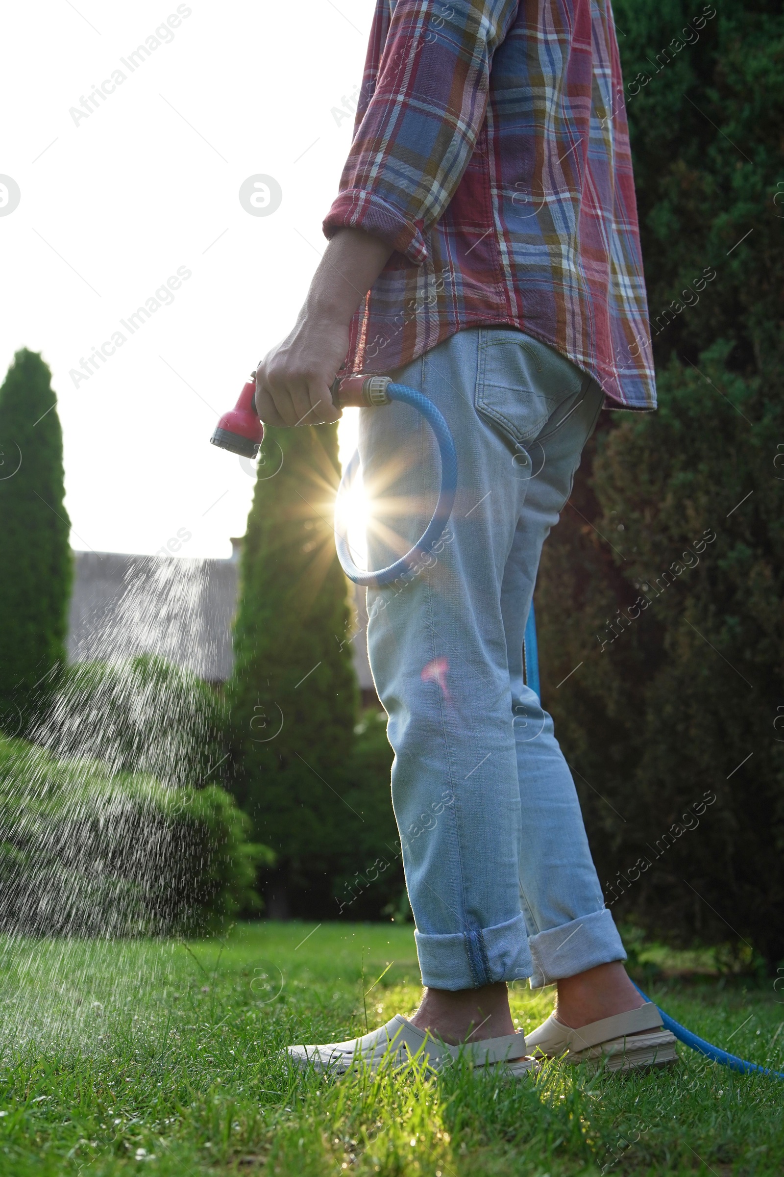 Photo of Man watering green grass on lawn in backyard, closeup