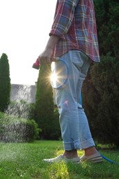 Photo of Man watering green grass on lawn in backyard, closeup