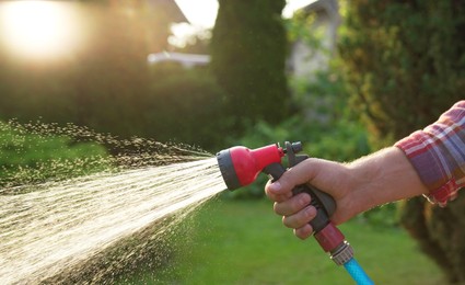 Photo of Man watering lawn with hose in backyard, closeup