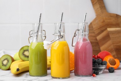 Glass bottles of tasty smoothies and different products on white marble table