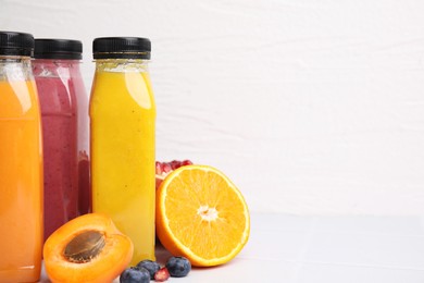 Glass bottles of tasty smoothies and different products on white tiled table, space for text