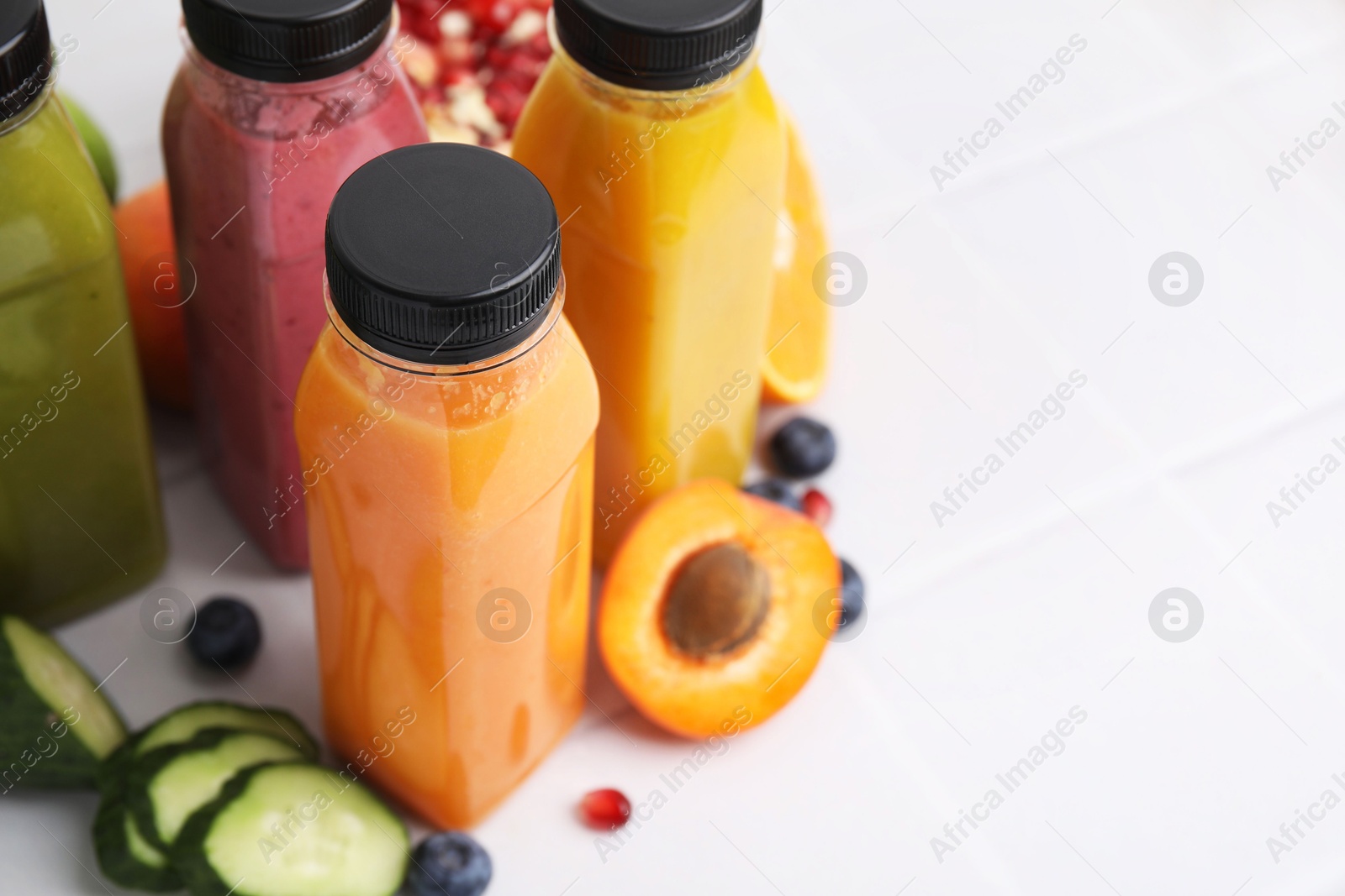 Photo of Glass bottles of tasty smoothies and different products on white tiled table, closeup. Space for text