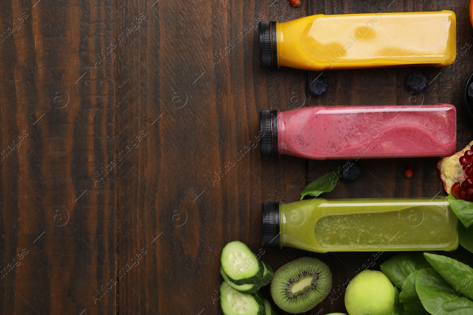 Photo of Glass bottles of tasty smoothies and different products on wooden table, flat lay. Space for text