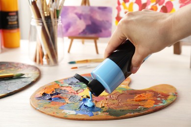 Photo of Woman mixing paints on palette at wooden table indoors, closeup