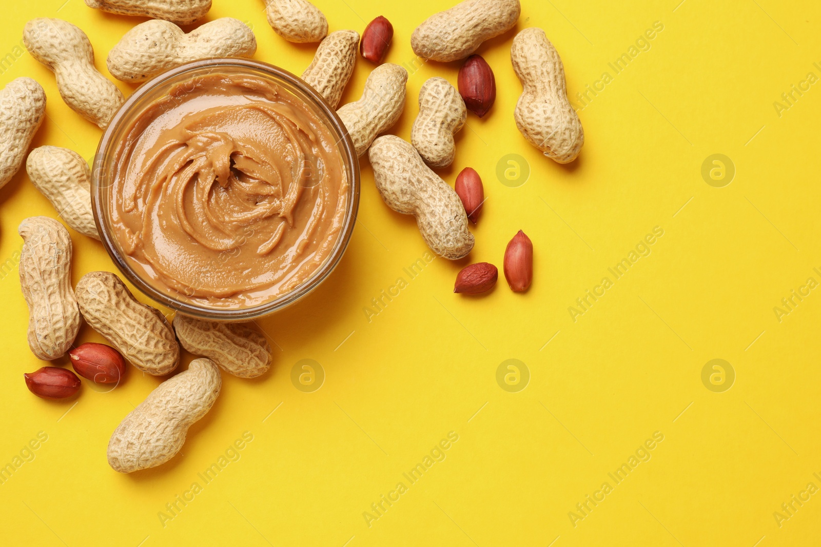 Photo of Tasty peanut butter in bowl and groundnuts on yellow table, flat lay. Space for text