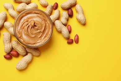 Tasty peanut butter in bowl and groundnuts on yellow table, flat lay. Space for text