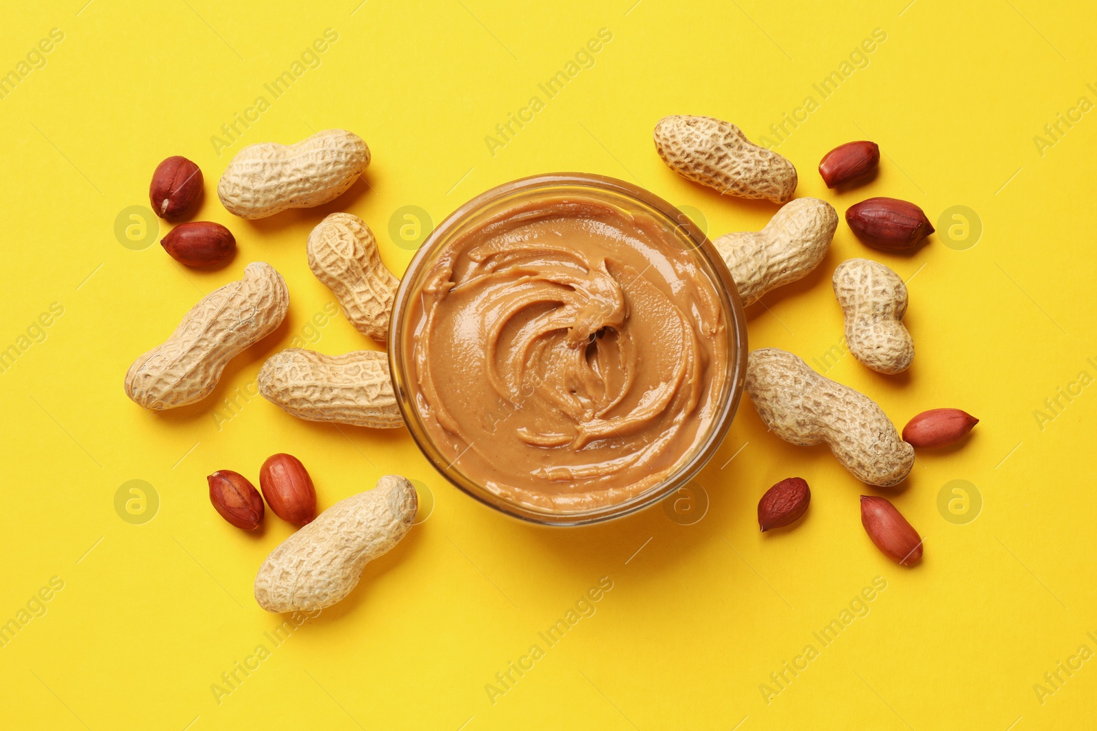 Photo of Tasty peanut butter in bowl and groundnuts on yellow table, flat lay