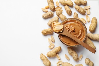 Tasty peanut butter in bowl and spoon with groundnuts on white table, flat lay. Space for text