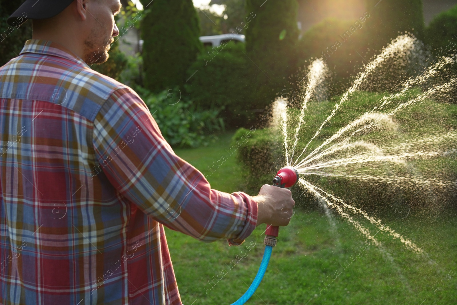 Photo of Man watering lawn with hose in backyard