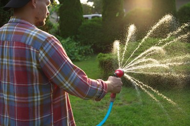 Photo of Man watering lawn with hose in backyard