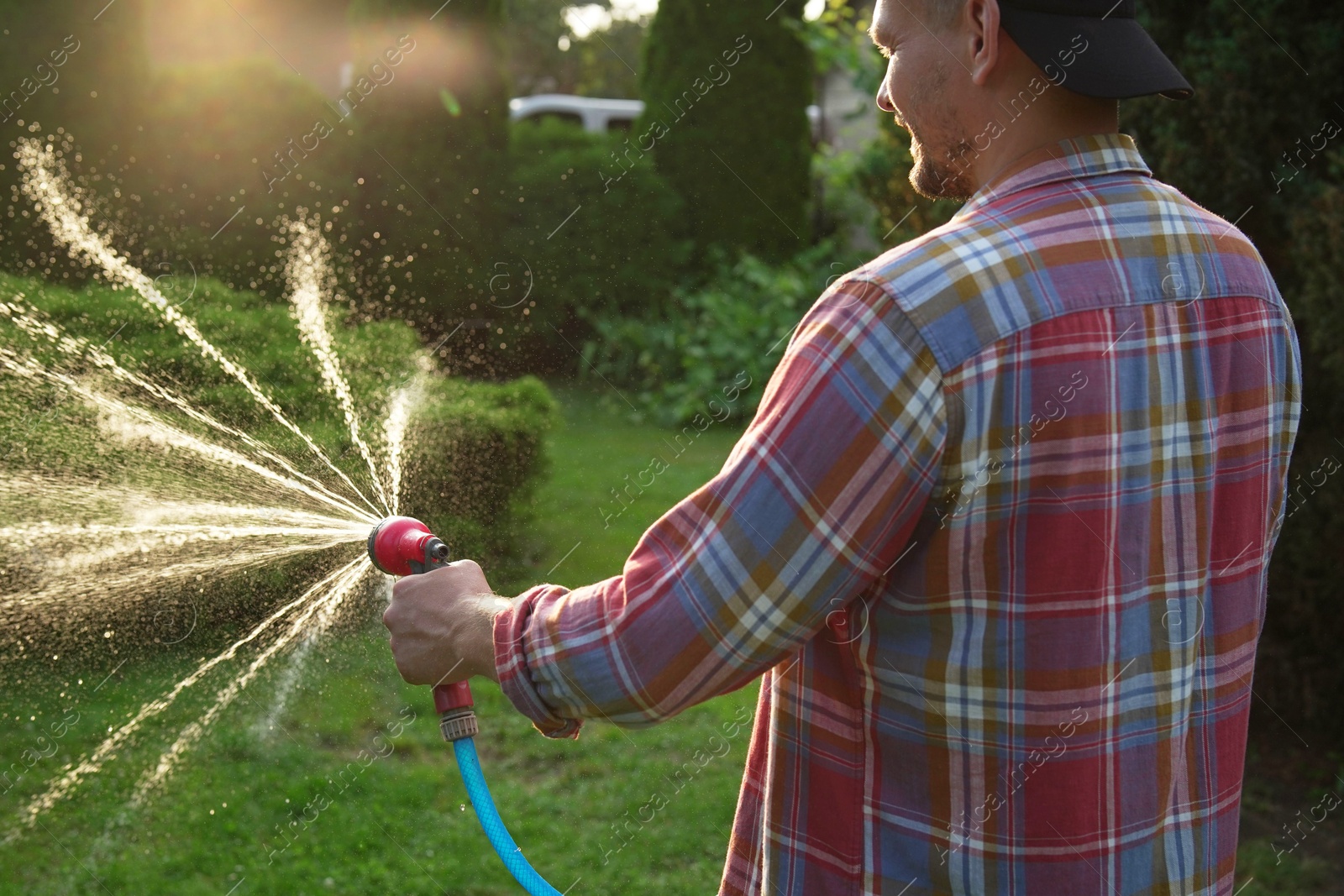 Photo of Man watering lawn with hose in backyard