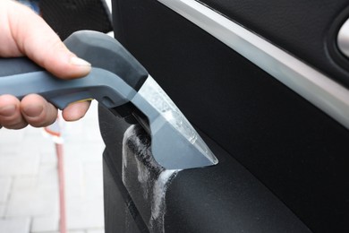 Photo of Man cleaning car door with vacuum cleaner outdoors, closeup