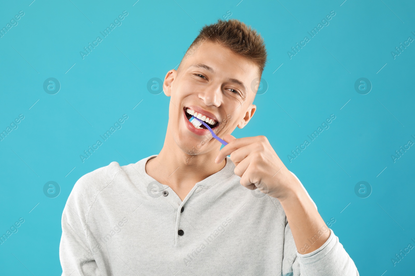 Photo of Young man brushing his teeth on light blue background