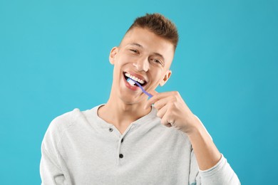 Young man brushing his teeth on light blue background