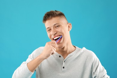 Young man brushing his teeth on light blue background