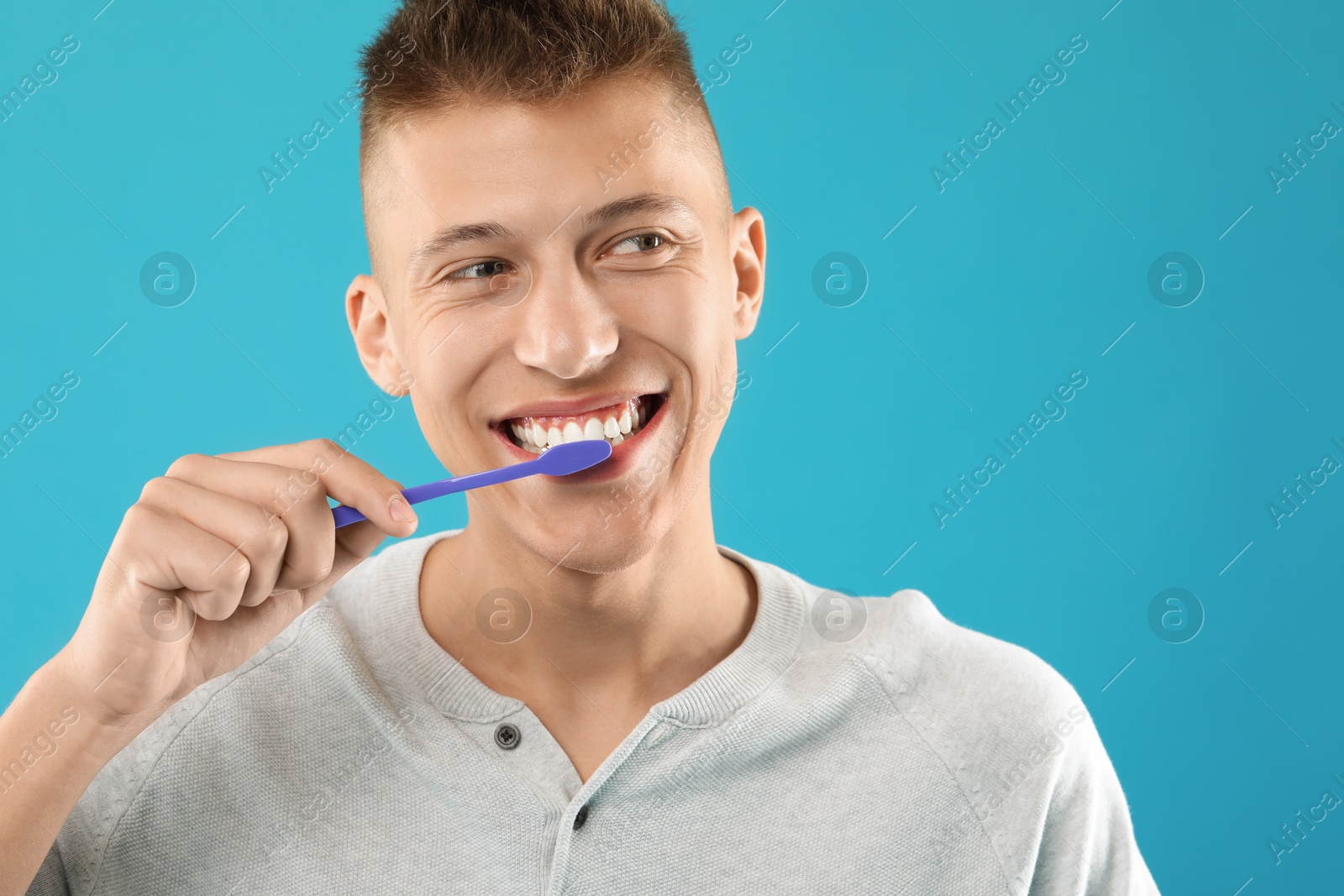 Photo of Young man brushing his teeth on light blue background, space for text