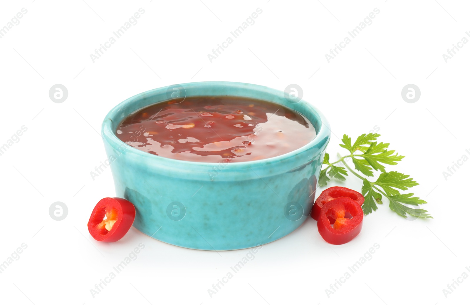 Photo of Hot chili sauce in bowl, parsley and cut pepper isolated on white