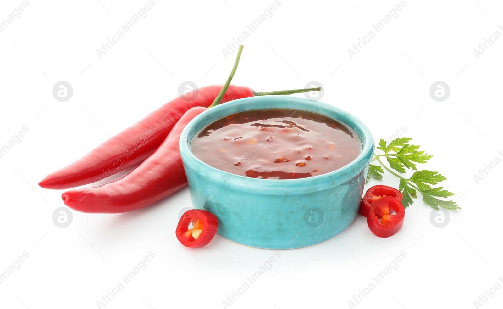 Photo of Hot chili sauce in bowl, parsley and peppers isolated on white